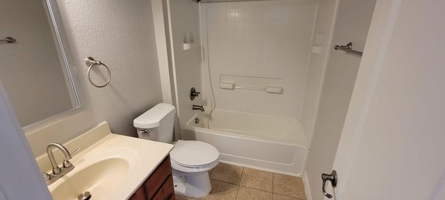 Bathroom featuring shower / tub combination, vanity, a textured wall, and light tile patterned floors | Image 13