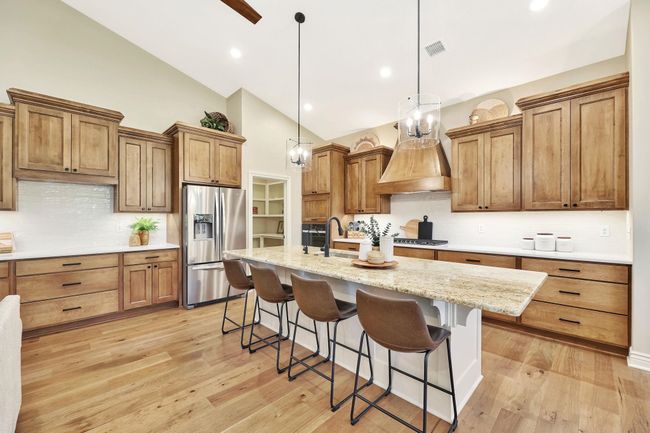 Kitchen with pendant lighting, light wood-type flooring, stainless steel refrigerator with ice dispenser, a kitchen island with sink, and a chandelier | Image 11