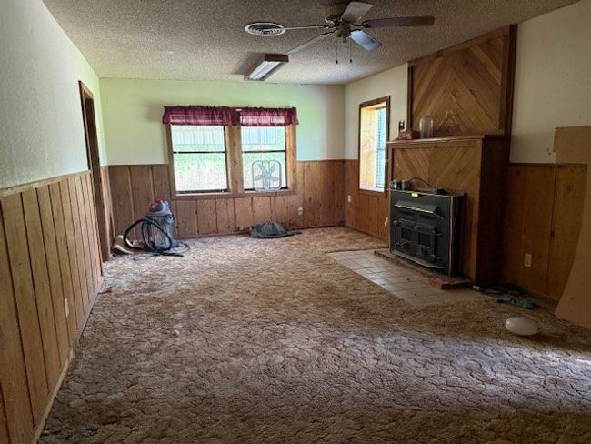 Unfurnished Bedroom featuring a wainscoted wall, wooden walls, a ceiling fan, a textured ceiling, and a wood​​‌​​​​‌​​‌‌​‌‌​​​‌‌​​‌‌​‌​​​​​‌ stove | Image 7