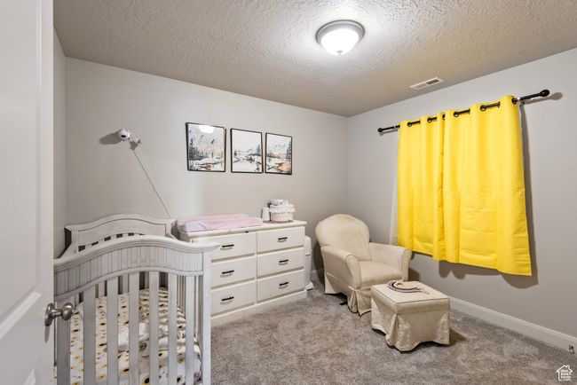 Carpeted bedroom featuring a nursery area, visible vents, a textured ceiling, and baseboards | Image 13