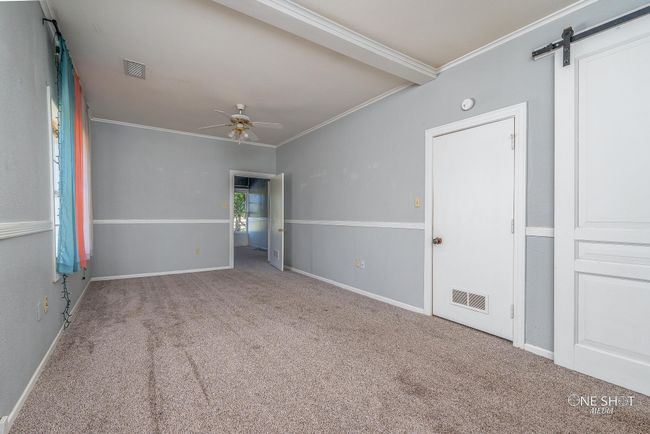 Carpeted empty room featuring ceiling fan, beamed ceiling, crown molding, and a barn door | Image 18