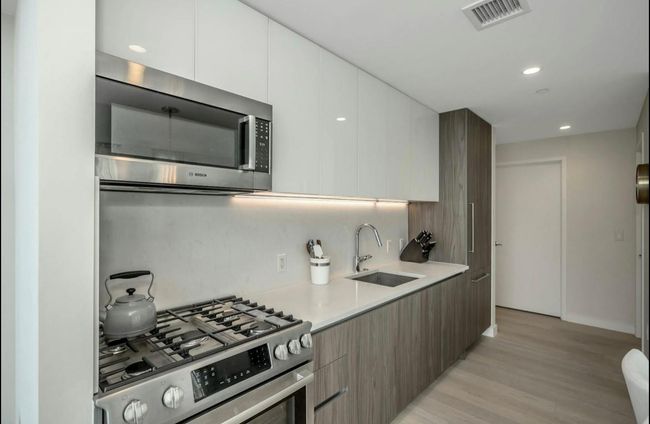 Kitchen featuring stainless steel appliances, modern cabinets, light countertops, light wood finished floors, and recessed lighting | Image 9