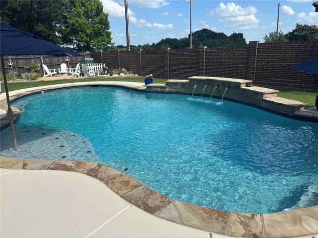 View of swimming pool featuring a stone wall with waterfall | Image 4