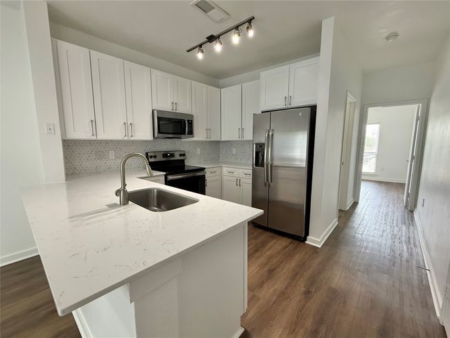 Kitchen featuring appliances with stainless steel finishes, a sink, a peninsula, dark wood-style floors, and white cabinetry | Image 4