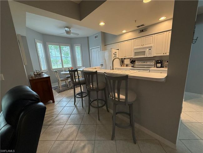 Kitchen featuring white appliances, a breakfast bar, light tile patterned flooring, white cabinetry, and light countertops | Image 5