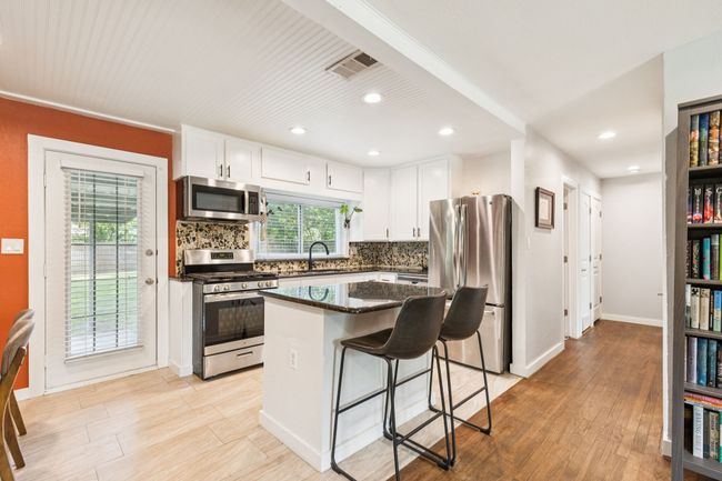 Kitchen featuring appliances with stainless steel finishes, tasteful backsplash, white cabinetry, a center island, and a breakfast bar area | Image 10