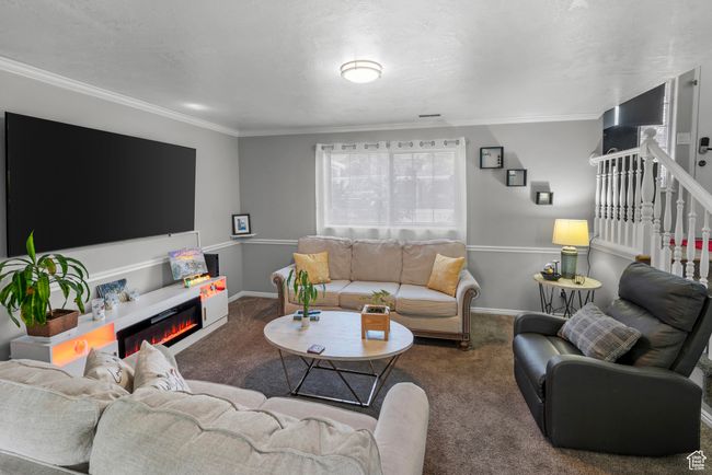 Carpeted living room featuring ornamental molding, stairs, and a glass covered fireplace | Image 5