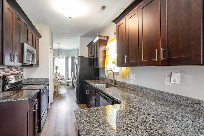 Kitchen featuring stainless steel appliances, dark stone countertops, wood finished floors, backsplash, and dark brown cabinets | Image 9