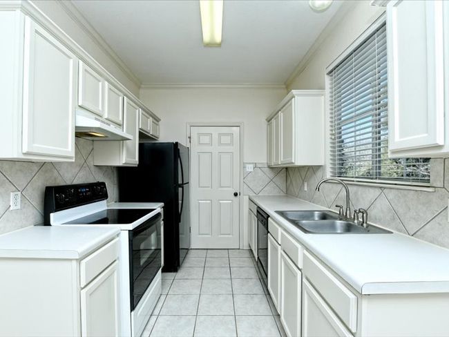Kitchen with light countertops, under cabinet range hood, electric stove, a sink, and light tile patterned floors | Image 8