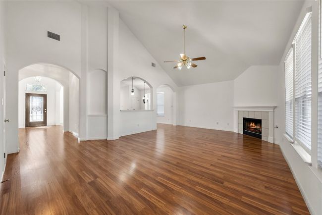 Unfurnished living room with arched walkways, visible vents, a tile fireplace, and wood finished floors | Image 5