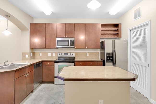 Kitchen with decorative light fixtures, stainless steel appliances, light countertops, and open shelves. All new paint. | Image 5