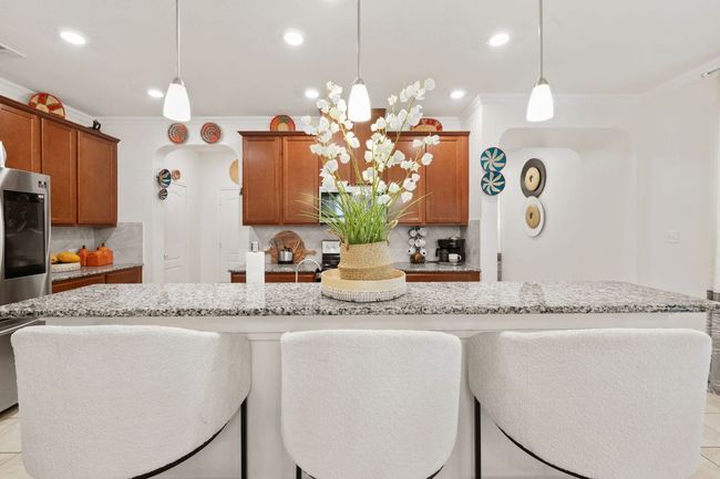Kitchen featuring ornamental molding, brown cabinetry, decorative backsplash, light stone countertops, and recessed lighting | Image 10