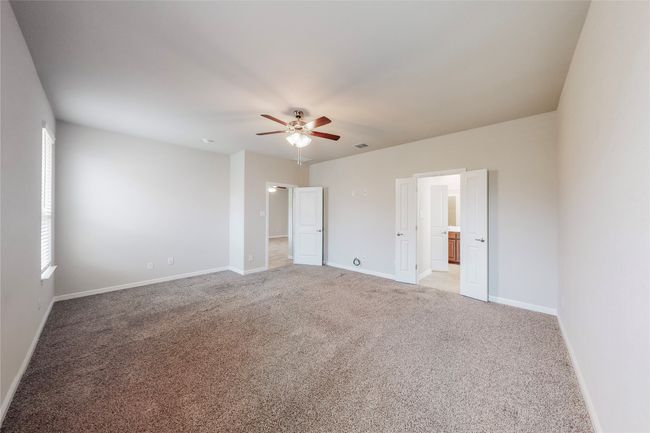 Unfurnished bedroom featuring light colored carpet, baseboards, a ceiling fan, and ensuite bath | Image 16