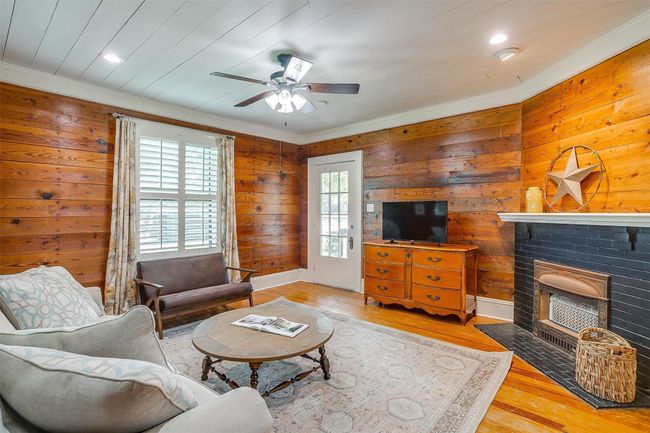 Living area with a ceiling fan, crown molding, wood finished floors, a brick fireplace, and wood walls | Image 12