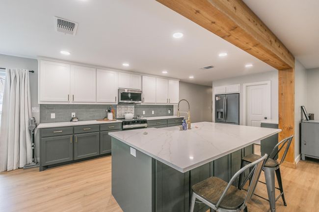 Kitchen featuring stainless steel appliances, light wood-type flooring, tasteful backsplash, white cabinets, and light stone countertops | Image 4