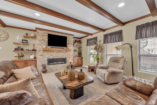 Carpeted living area with beam ceiling, crown molding, a stone fireplace, baseboards, and recessed lighting | Image 7