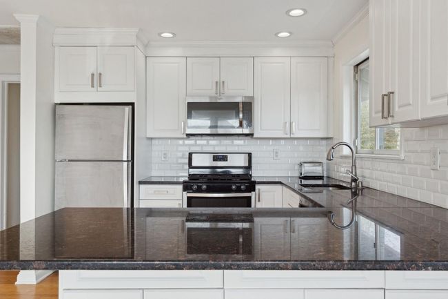 Kitchen with white cabinets, stainless steel appliances, a peninsula, a sink, and dark stone counters | Image 9