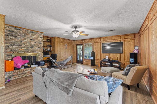 Living area featuring ceiling fan, light wood-style flooring, a fireplace, wooden walls, and crown molding | Image 13