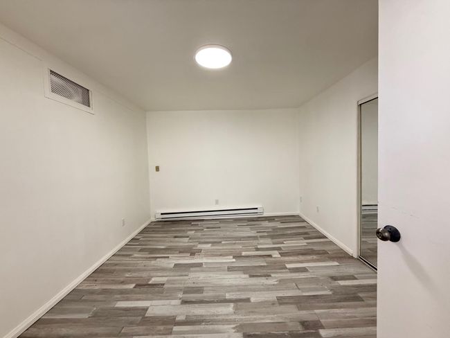 bedroom with a baseboard radiator, wood finished floors, baseboards, and visible vents | Image 10