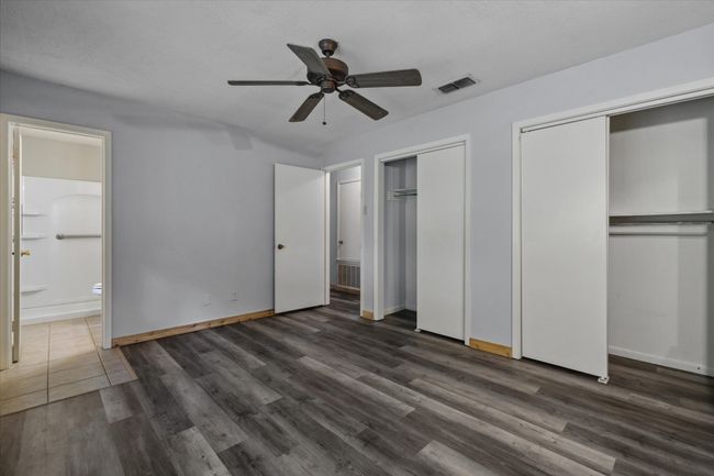 Unfurnished bedroom featuring multiple closets, ensuite bathroom, wood finished floors, and ceiling fan | Image 8