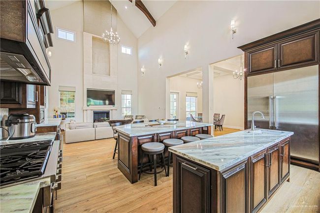 Kitchen with built in fridge, a chandelier, high vaulted ceiling, and open floor plan, brazilian stone countertops one large seating island(seats 10) and one large prep island with vegetable sink | Image 17