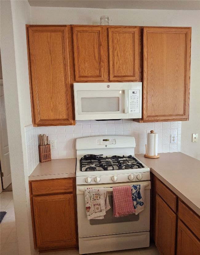 Kitchen featuring light countertops, backsplash, brown cabinetry, and white appliances | Image 7