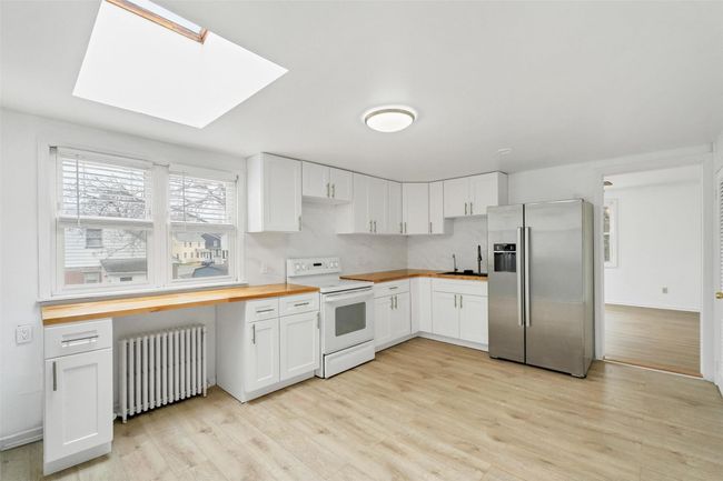 Kitchen with butcher block counters, radiator heating unit, a skylight, stainless steel refrigerator with ice dispenser, and electric stove | Image 7