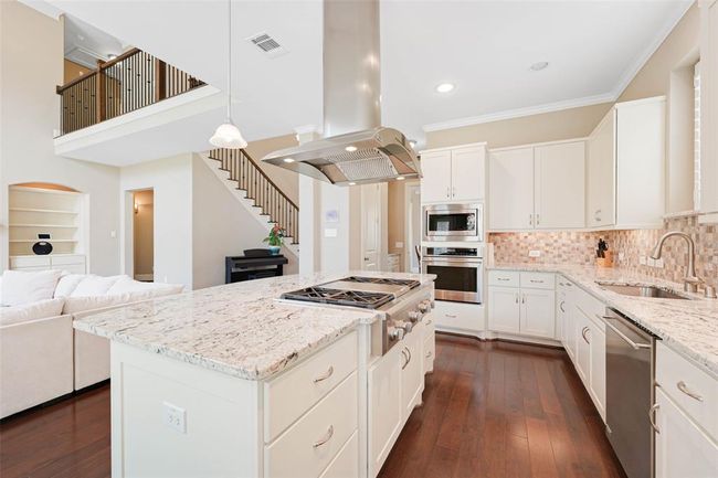 Stylish kitchen with granite countertops, custom cabinetry, and stainless steel appliances—including double ovens and a gas cooktop on the island. | Image 13