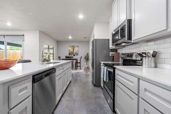 Kitchen featuring a sink, tasteful backsplash, finished concrete floors, light countertops, and appliances with stainless steel finishes | Image 7
