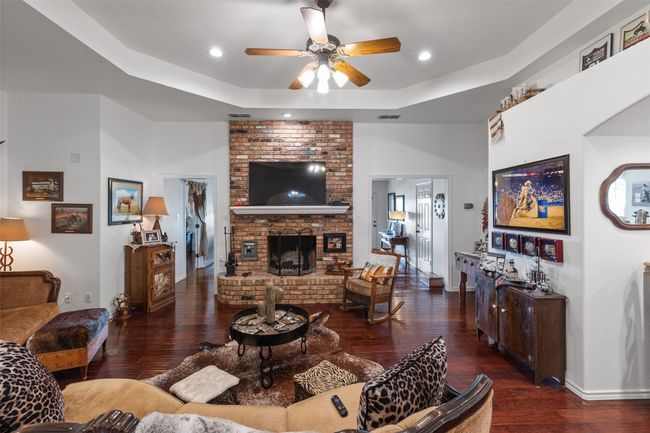 Living room with visible vents, a raised ceiling, a brick fireplace, ceiling fan, and wood finished floors | Image 5