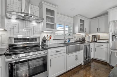 Kitchen featuring wine cooler, dark wood-type flooring, wall chimney exhaust hood, appliances with stainless steel finishes, and decorative backsplash | Image 1