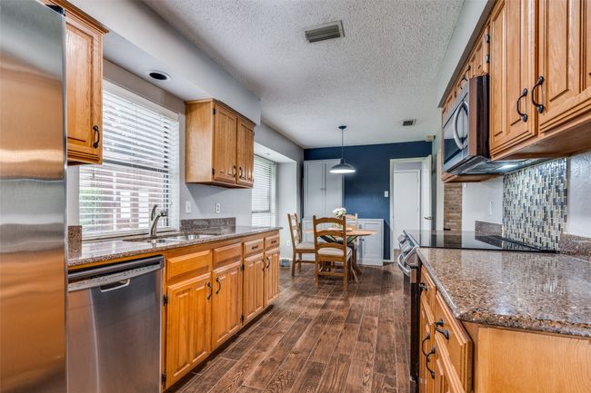 Kitchen featuring appliances with stainless steel finishes, dark wood-style flooring, brown cabinetry, dark stone counters, and a textured ceiling | Image 12