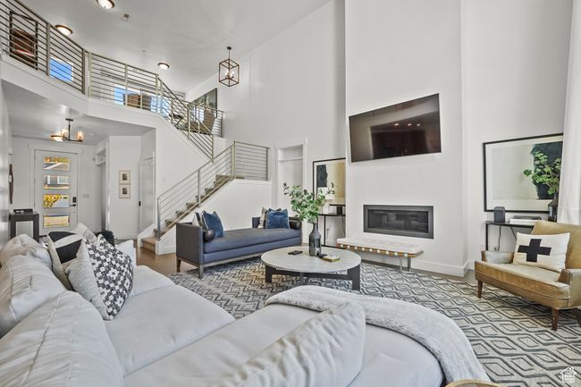 Living area featuring a chandelier, a towering ceiling, stairway, and a glass covered fireplace | Image 9