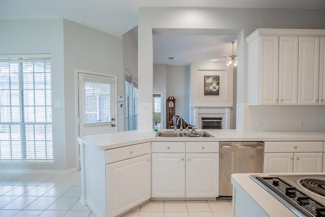 Bright kitchen with white cabinetry and countertops. Open layout connects to a living area with a fireplace. Large windows provide ample natural light, and there's access to the backyard through a side door. | Image 22