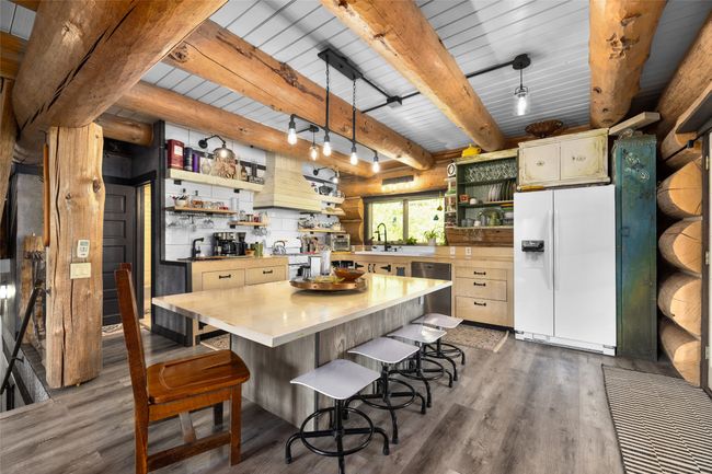 Kitchen with open shelves, white fridge with ice dispenser, dark wood finished floors, light countertops, and beam ceiling | Image 4