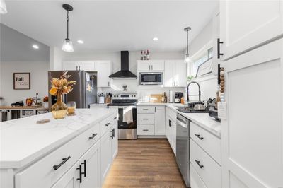 Kitchen featuring white cabinetry, sink, appliances with stainless steel finishes, dark wood-type flooring, and wall chimney range hood | Image 1