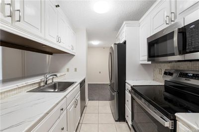 Kitchen with light tile patterned floors, light stone counters, stainless steel appliances, white cabinetry, and sink | Image 1