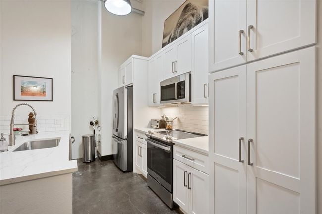Kitchen featuring appliances with stainless steel finishes, backsplash, white cabinetry, and concrete flooring | Image 8