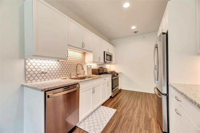 Kitchen with stainless steel appliances, light wood finished floors, backsplash, white cabinetry, and recessed lighting | Image 6