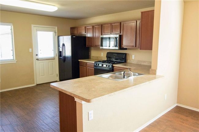 Kitchen featuring black appliances, light countertops, brown cabinetry, and wood finished floors | Image 4