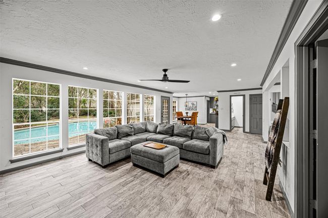 This spacious living area features large windows overlooking a pool, offering plenty of natural light. The room has modern tile flooring and flows seamlessly into a dining space and kitchen, creating an ideal open-concept layout and perfect flow between rooms. | Image 9