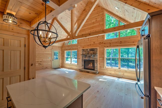 Unfurnished living room with a chandelier, wood ceiling with exposed beams, wood walls, light wood-style floors, and high vaulted ceiling | Image 17