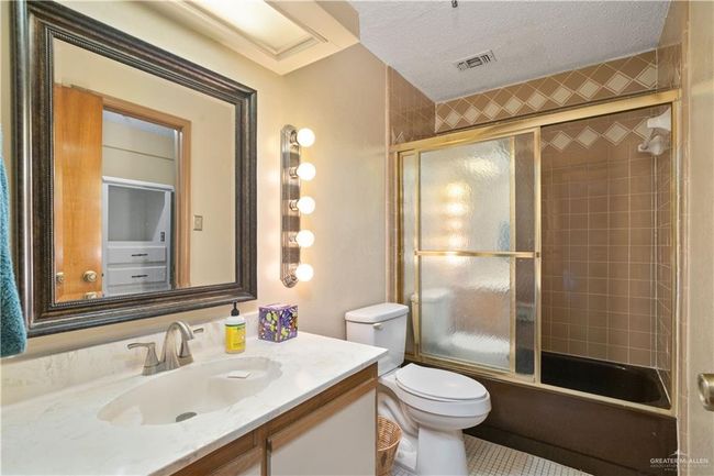Full bath featuring vanity, bath / shower combo with glass door, and a textured ceiling | Image 16