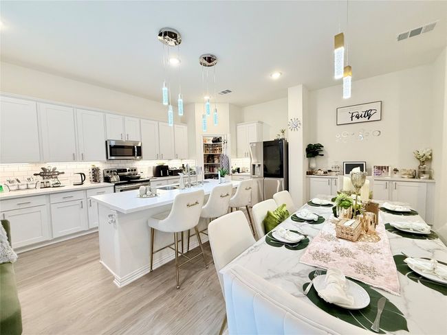 Kitchen featuring stainless steel appliances, backsplash, a breakfast bar area, light countertops, and a kitchen island with sink | Image 5