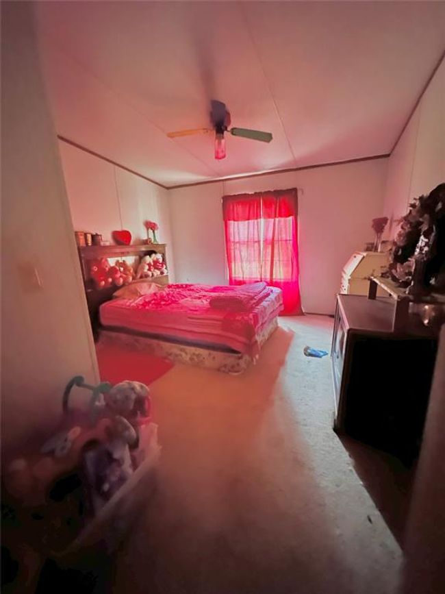 Cozy bedroom with soft lighting, featuring a large bed and a window with red curtains. There's a colorful ceiling fan and ample space for personal items, creating a warm and inviting atmosphere. | Image 9