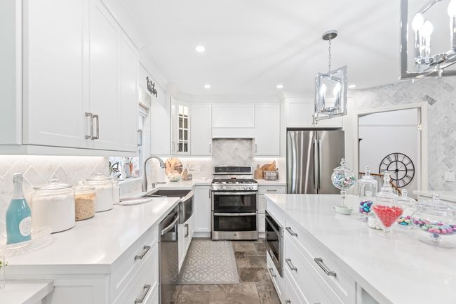 Kitchen with stainless steel appliances, a sink, light countertops, white cabinetry, and premium range hood | Image 13