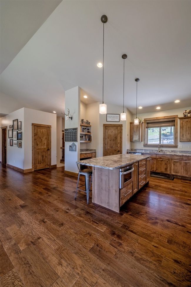 Kitchen featuring brown cabinets, dark wood-style flooring, a sink, a center island, and light stone countertops | Image 11