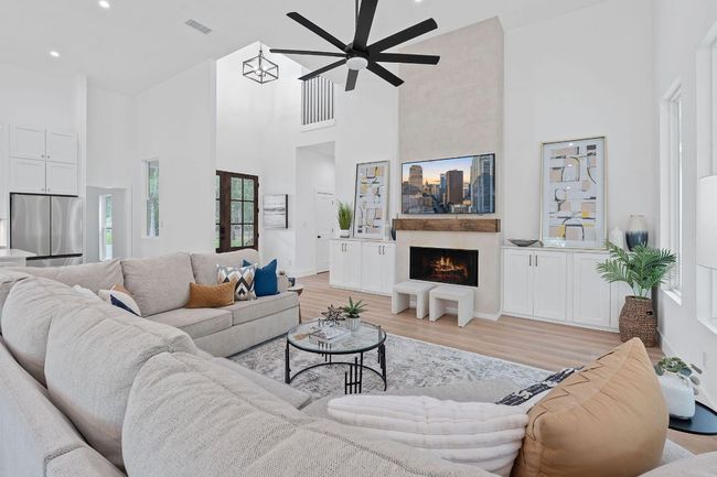 Living room with high vaulted ceiling, light wood-style flooring, a ceiling fan, and a lit fireplace | Image 9