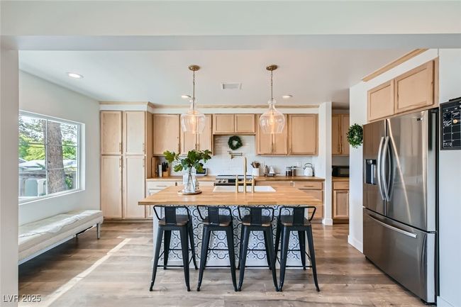 Kitchen with stainless steel fridge with ice dispenser, light brown cabinets, a breakfast bar, light wood-type flooring, and recessed lighting | Image 12