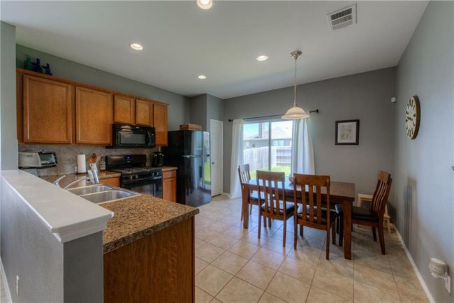 Kitchen featuring black appliances, brown cabinetry, decorative backsplash, a sink, and baseboards | Image 4
